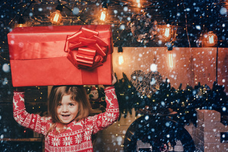 Christmas eve and magic concept. Bright New Years interior. The concept of giving and receiving gifts. Cheerful smiling happy little cute girl holding gigantic gift present from Santa.の写真素材