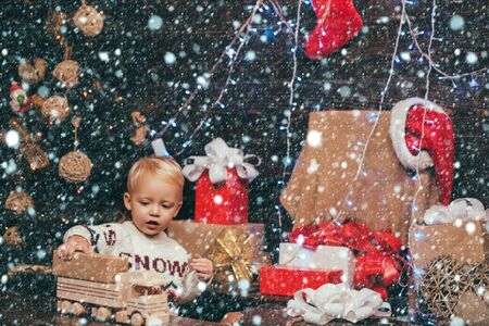 Happy little child dressed in winter clothing think about Santa near Christmas tree. Kid in snow. Merry Christmas and Happy New year. The morning before Xmas.の写真素材