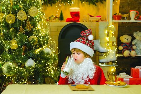 Santa picking cookie and glass of milk. Little Santa Claus helper drinking milk on Christmas Eve....