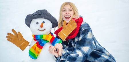 Funny Girl Love winter. Outdoor portrait of young pretty beautiful woman in cold sunny winter weather in park. Winter waman with Snowman on snow background.の写真素材