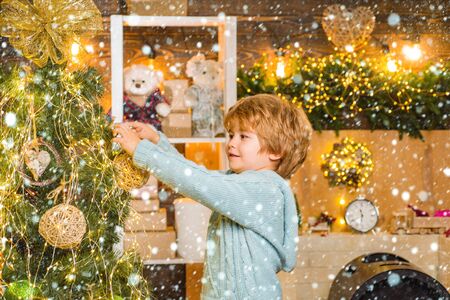 Happy child holding Christmas bauble in front of Christmas tree. Little child boy is happy about the New Year. Christmas preparation. Child in snow.の写真素材