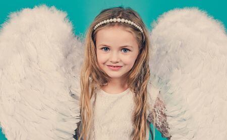 Wonderful blonde little girl in the image of an angel with white wings. Angel kid with blonde curly hair. Angel. Beautiful child angel posing and looking at camera.の写真素材