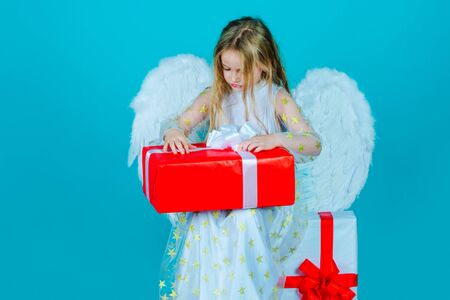 Valentines Day. Little angel girl open gift. Cute child girl posing with angel wings. Beautiful little angel. Angel child from heaven gives you gift.の写真素材