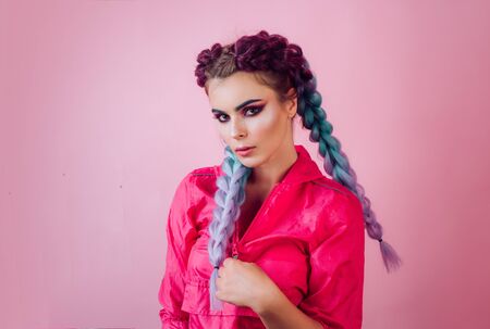 Beautiful stylish girl with colorful kanekalon braided in her hair. Pretty woman with colorful violet ombre hair and pro makeup isolated at pink background. Hairdresser salon concept.の写真素材