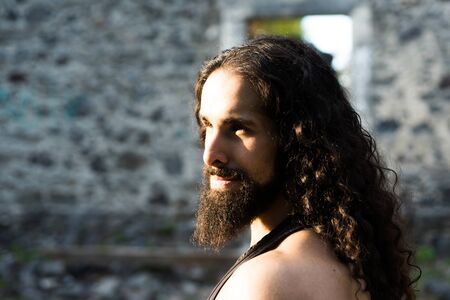 Handsome bearded man with long dark hair. Man style and fashion concept. Close up portrait of handsome man with long dark wavy hair and beard. Confident man with unusual appearance stare straight before one.の写真素材