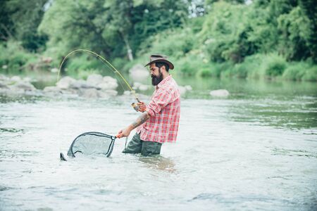 Elegant bearded brutal hipster man fishing. Fishing requires to be mindful and fully present in moment. Successful catch. Strategy. Fly fishing. Keep calm and fish on. Make with inspiration.の写真素材
