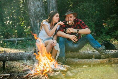 Good day for spring picnic in nature. Vacation weekend picnic camping and hiking. Company friends picnic or barbecue near bonfire. Funny couple roasting marshmallows on campfire.の写真素材
