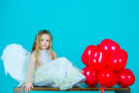 Kids Valentines Day. Wonderful blonde little girl in the image of an angel with white wings. Beautiful young girl wearing angel wings. Child angel with a beautiful wings.の写真素材