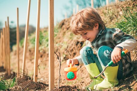 Happy Kid with Shovel and watering can. Watering flowers in garden.の写真素材