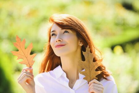 Romantic looking cute girl walking outdoor. Pretty woman playing with oak leaves. Woman with...
