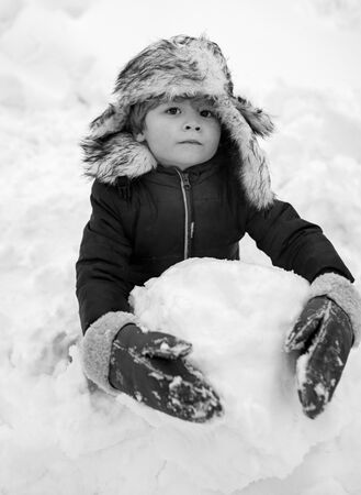 Cute kid - winter portrait. Outdoor portrait of little son in cold sunny winter weather in park. Making snowman and winter fun for children. Happy winter time.の写真素材