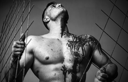 Muscular man nude torso soiled blood. Halloween concept. Scary monster just murdered his victim. Strong aggressive monster behind grid. Prison for monster. Psycho mad man. Murderer mythical creatureの写真素材