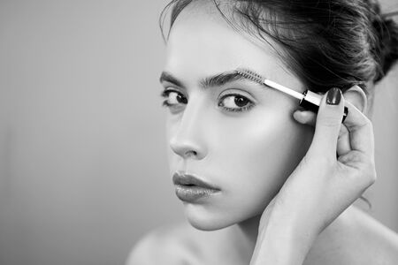 Care eyebrow. Makeup artist applying a brow gel on the eyebrows of a young beautiful woman with flawless nude natural makeup. Concept of professional make up doing.の写真素材