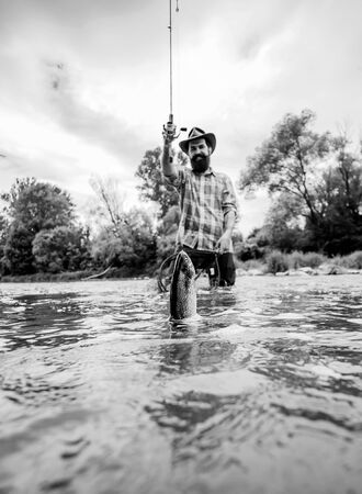 Man fishing and relaxing while enjoying hobby. Happy fisherman fishing in river holding fishing...