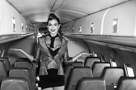 Beautiful flight attendant in an airplane cabin smiling. Charming stewardess dressed in blue uniform. Travel concept. Attractive young woman flight attendant stewardess. Airplane onboard.の写真素材