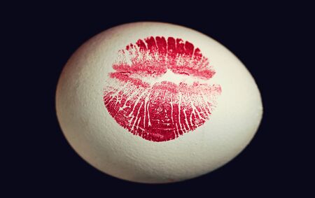 Red lip imprint on easter egg on black background. Print of red lips on white egg. Egg huntの写真素材
