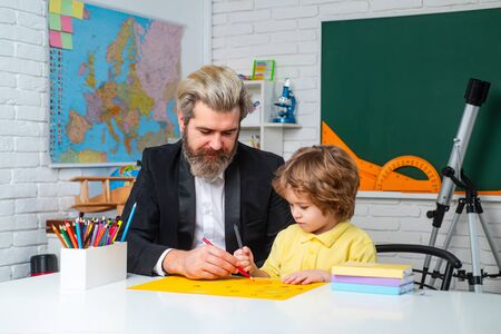 Father teaching son. Funny little child with father having fun on blackboard background. Supporting pupils at school. Private kids tutoring.の写真素材