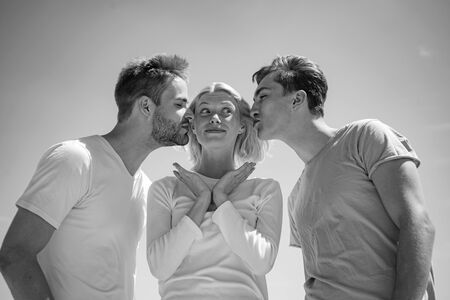 Company of happy young people spend leisure outdoors at sky background. Brothers kissing their...