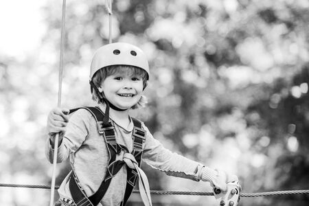 Children summer activities. Adventure climbing high wire park. Cute baby boy playing. Hiking in the rope park girl in safety equipment. Happy child climbing in the trees. Child.の写真素材