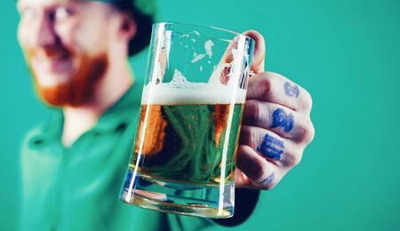 Portrait of excited man holding glass of beer on St Patrick's day isolated on greenの写真素材
