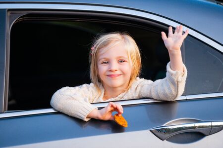 A little girl is sticking her head out the car window. Road trip or travel concept. Happy kids...