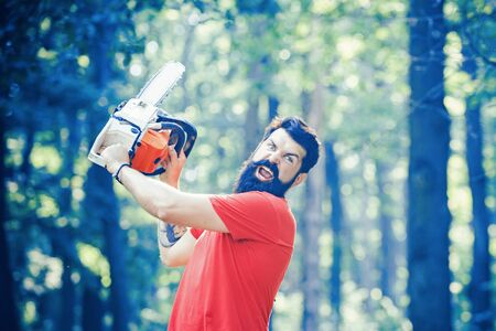 Lumberjack holding the chainsaw. Deforestation is a major cause of land degradation and destabilization of natural ecosystems. Handsome young man with axe near forest.の写真素材