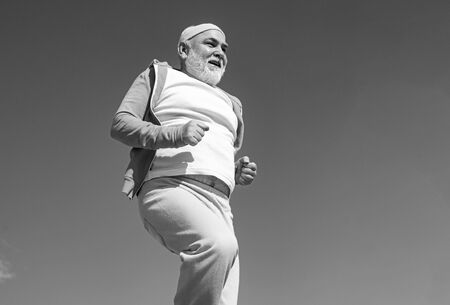Elderly man practicing sports on blue sky background. Cheerful senior jogging in sportswear on sky background. Age is no excuse to slack on your health.の写真素材