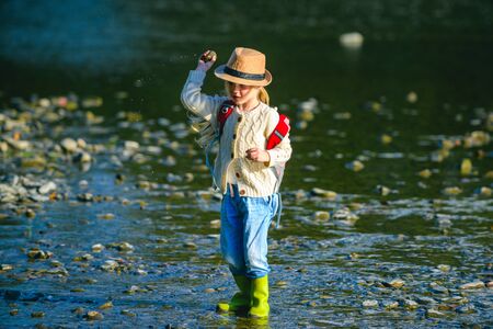 Little girl throw stones at the Stony river. Beautiful kids girl throws a rock at the river....