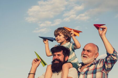 Kids playing with simple paper planes on sunny day. Father giving son ride on back in park. Generation concept. Child happy. Three men generation.の写真素材
