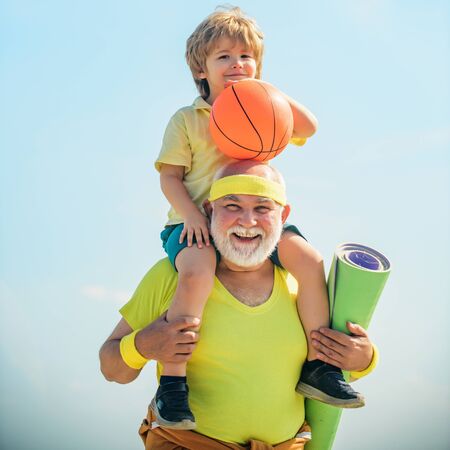 Sportsman grandfather and healthy kid with basketball ball on blue sky background. Grandfather and...