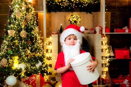 Cheerful cute child opening a Christmas present. Cute little child near Christmas tree. Kids enjoy the holiday. Christmas child holding a red gift box.の写真素材