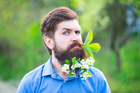 Funny Blossom beard. Spring fashion man outdoors portrait in blooming flowers in beard. Romantic man in flowers. Male model Enjoying Nature. Romantic beauty in fantasy orchard.の写真素材