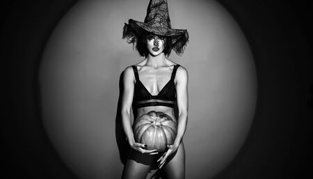 Halloween   Witch with a carved Pumpkin on red backgroung. Fantasy horror Halloween. Design for Halloween banner. Beautiful woman posing with pumpkin.の写真素材