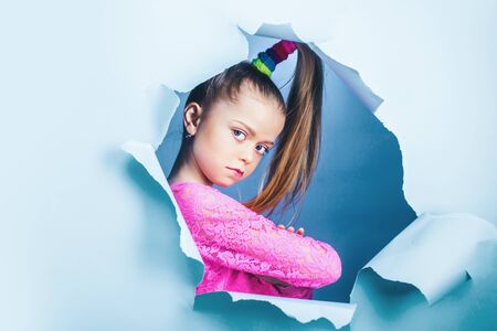 Serious child girl looking out of a paper hole. Banner. Happy girl.