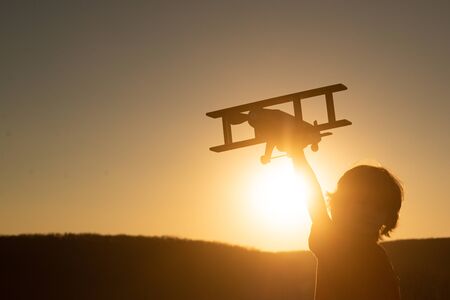 Kid child boy pilot aviator with airplane dreams of traveling in summer in nature at sunset