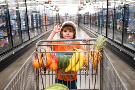Sale, consumerism and people concept - happy little boy with food in shopping cart at grocery store. Little boy in the supermarket.の写真素材