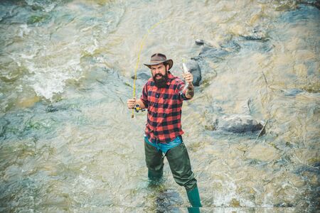 Angler catching the fish. Handsome fisherman in hat and red checkered shirt. Carry on fishing. Big...
