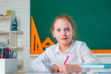 Little girl pupil with happy face expression near desk with school supplies. Learning concept. Happy...