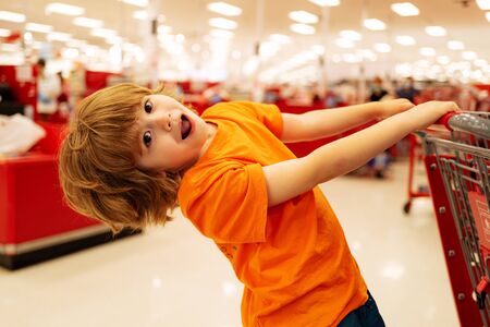 A boy is shopping in a supermarket. Funny child with shopping trolley with in grocery store.の写真素材