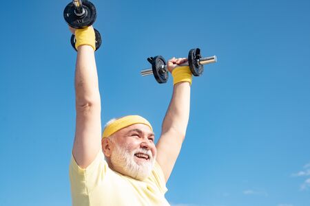 Old man holding his hands in front of him while lifting dumbbells. Senior sportman lifting dumbbells. Elderly man workout.の写真素材