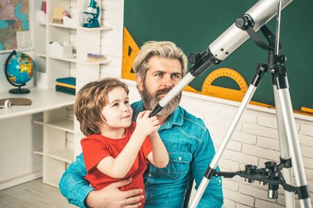 Father teaching son. Cute pupil with funny face hold Astronomy telescope.の写真素材