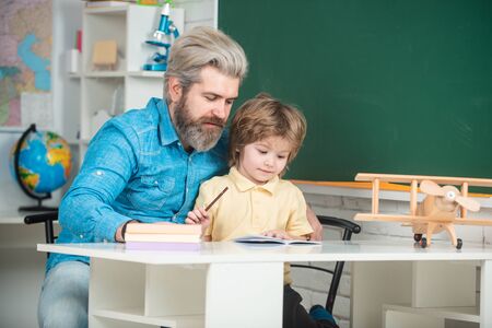 Cute child boy with teacher in classroom near blackboard desk. Pupil of primary school study indoors. Home school for pupil.の写真素材