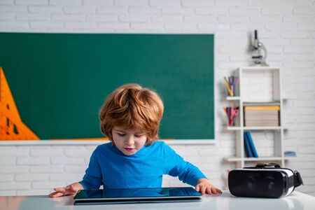 School child with tablet in school classroom. Portrait of Pupil in classroom. Cute child boy in classroom near blackboard desk.の写真素材