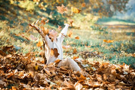 Autumn romantic mood. Autumn yellow leave in the girls hand. Fall woman portrait of happy lovely and beautiful young woman in forest in fall colors. Autumn girl playing in city parkの写真素材