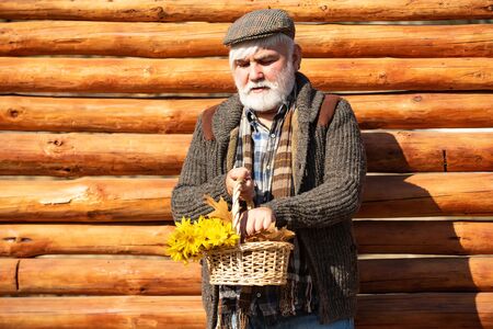 Old hipster man with flowers. Portrait of aged man with beard. Happy man with beard and mustache hold basket of flowers. Outdoor portrait. Wooden background.の写真素材