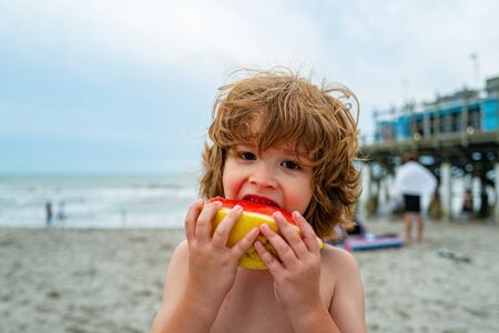 A child eats watermelon. Cute kid eat watermelon while standing on summer beach.の写真素材