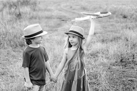 Little children - daughter and son is playing and dreaming of flying. Child care. Cute children - daughter and son playing with toy airplane in the meadow in vintage color tone.の写真素材