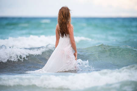 Young woman in nature with beautiful sea and blue sky. Summer vacation and travel concept. Dream and imagination. Sensual girl playing with Waves on blue sea.の写真素材
