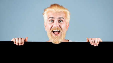 Man holding empty black blank board. Man holding blank paper board studio portrait. Young man shows a sheet of paper in the camera on a gray background.の写真素材