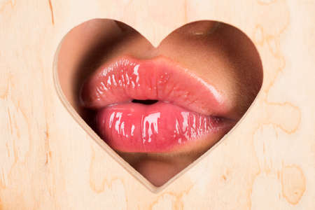 Lips in heart shape. Red lip with glossy lipgloss. Tongue and sexy. Close up, macro with beautiful mouths. Sexy kiss, sensual seductive lips of a young woman. Cosmetics and beauty salon.の写真素材